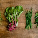 A vibrant selection of fresh herbs and greens neatly arranged on a wooden tabletop.