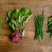 A vibrant selection of fresh herbs and greens neatly arranged on a wooden tabletop.