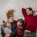 Smiling family of four lying on a blanket, sharing happiness and love indoors.