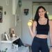 Smiling woman in activewear lifting dumbbells at home for a healthy lifestyle.