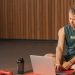 Man sitting on exercise mat with laptop, surrounded by dumbbells, creates a unique fitness workspace.